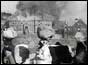 North Koreans with luggage on heads and burning building in background 