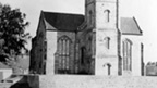 Church with central square tower standing in open fields.